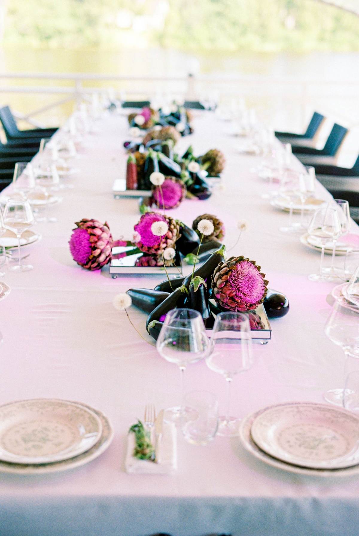 Et langt bord med lyserød dug, tallerkener og mørke og pink blomster