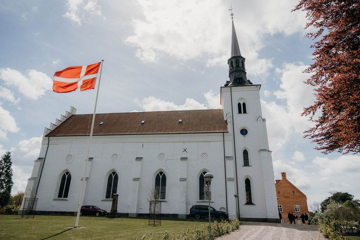 Hvid kirke med tårn og Dannebrog under blå himmel