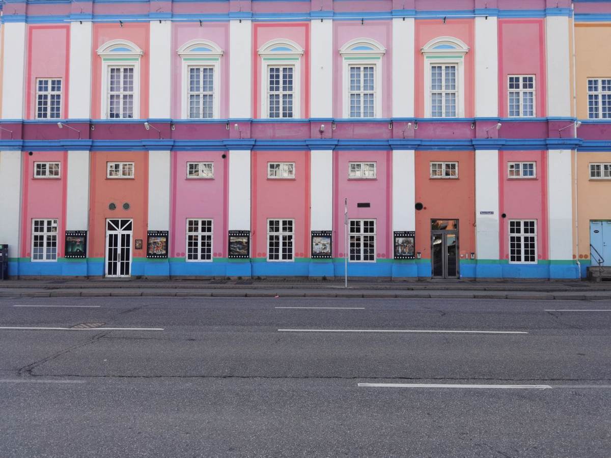 En lang lyserød og blå bygning med hvide pilastre set over en tom vej