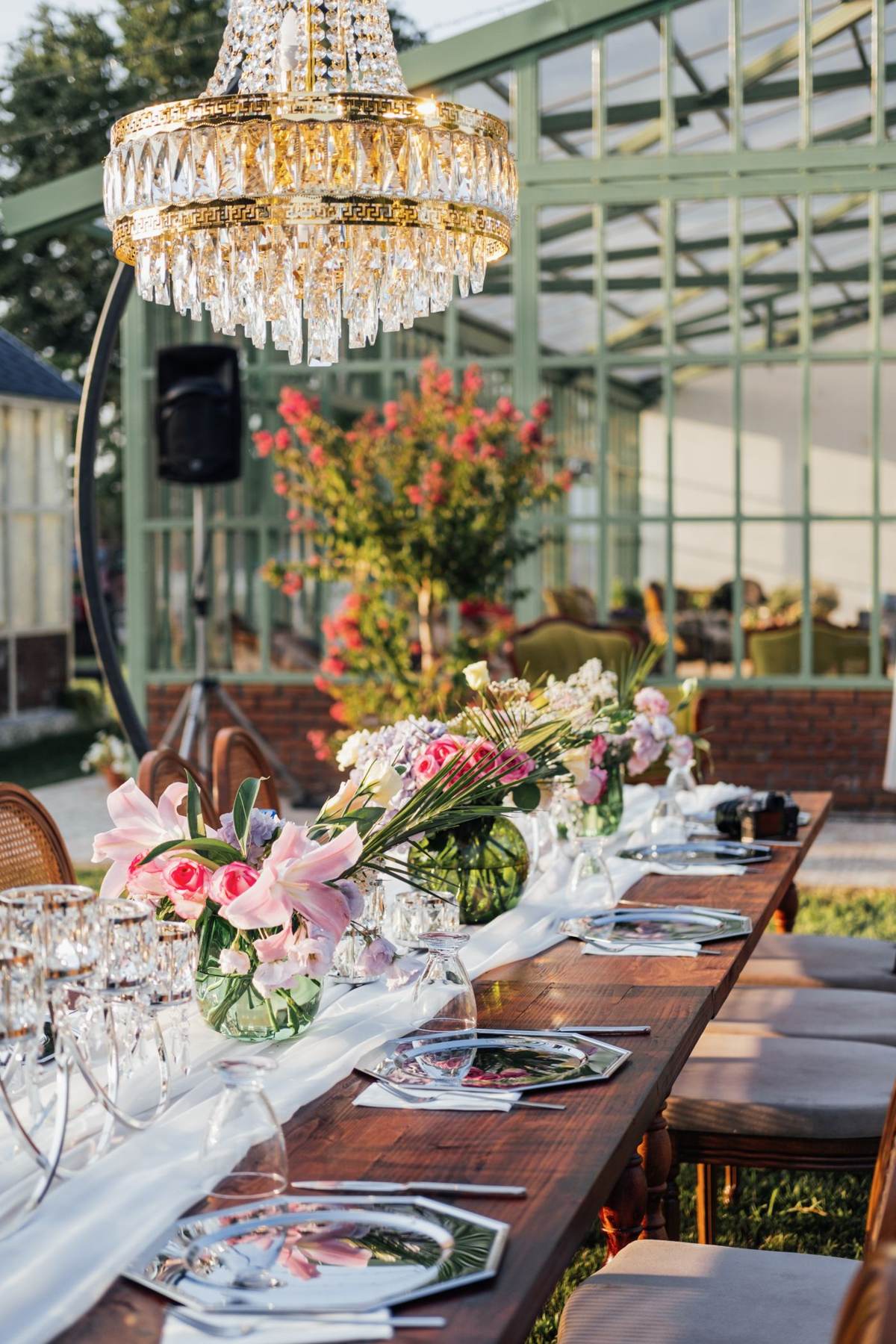 Et langt bord i et drivhus med blomster, glas og tallerkener
