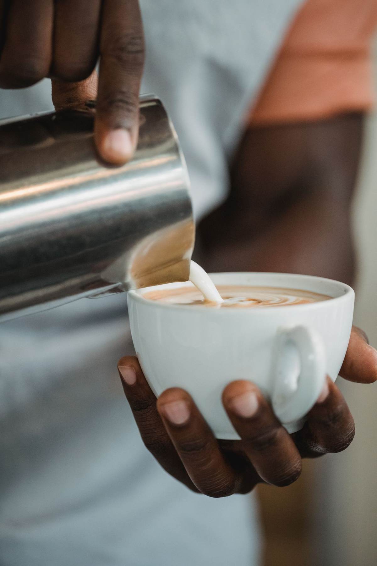 En barista holder en kop cappuccino og mælkekanden