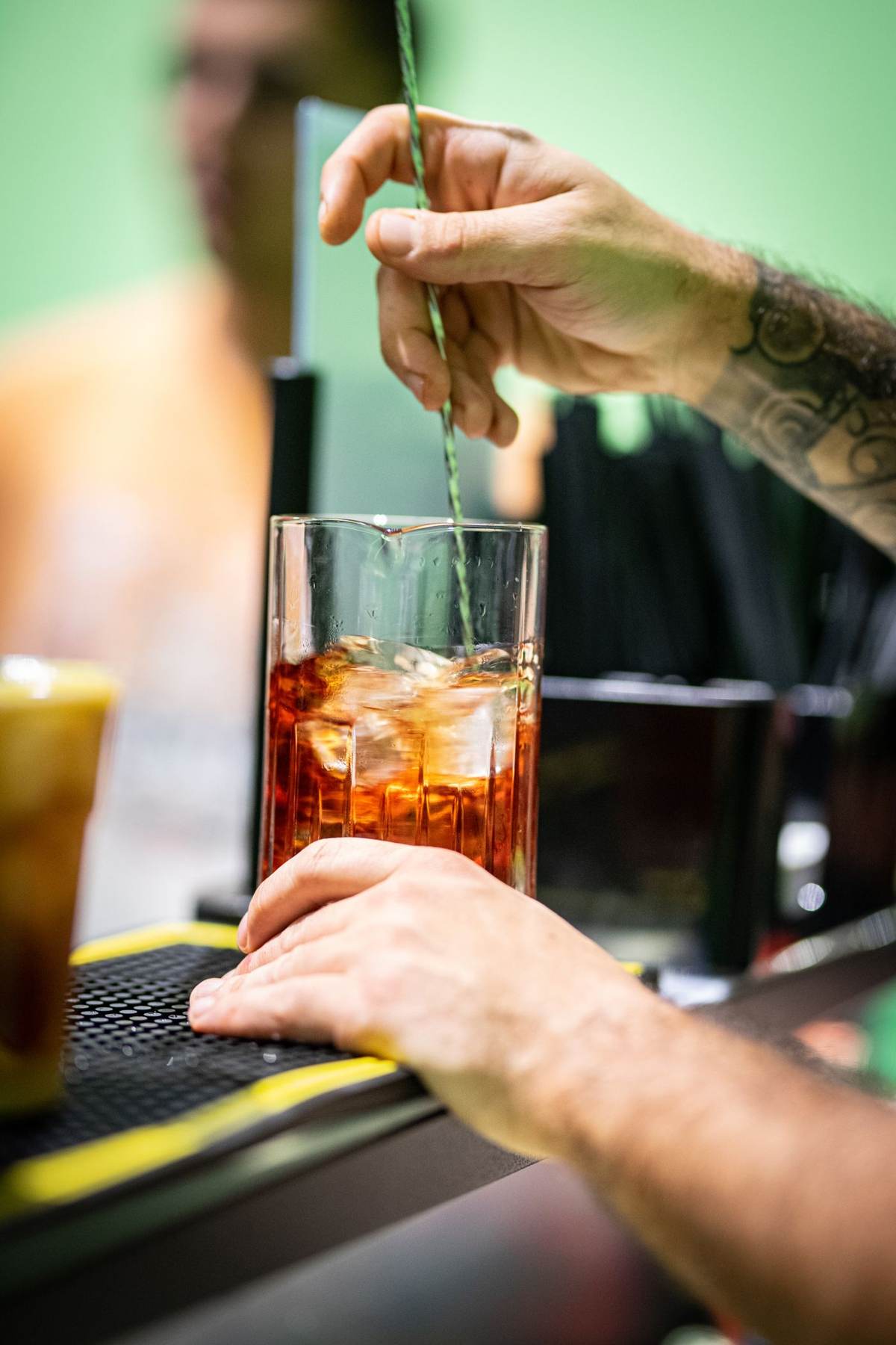 En hånd rører rundt i en cocktail på en bar