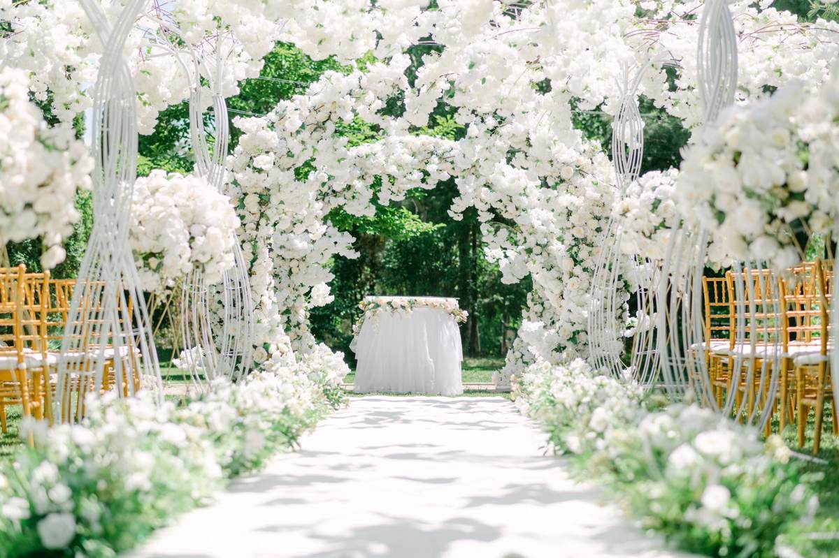 En lysegang mellem stole, kranset af hvide blomster og en blomsterbue