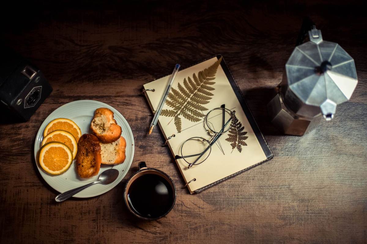 Morgenbord med kaffe, appelsinskiver, brød og en bog på mørkt træ