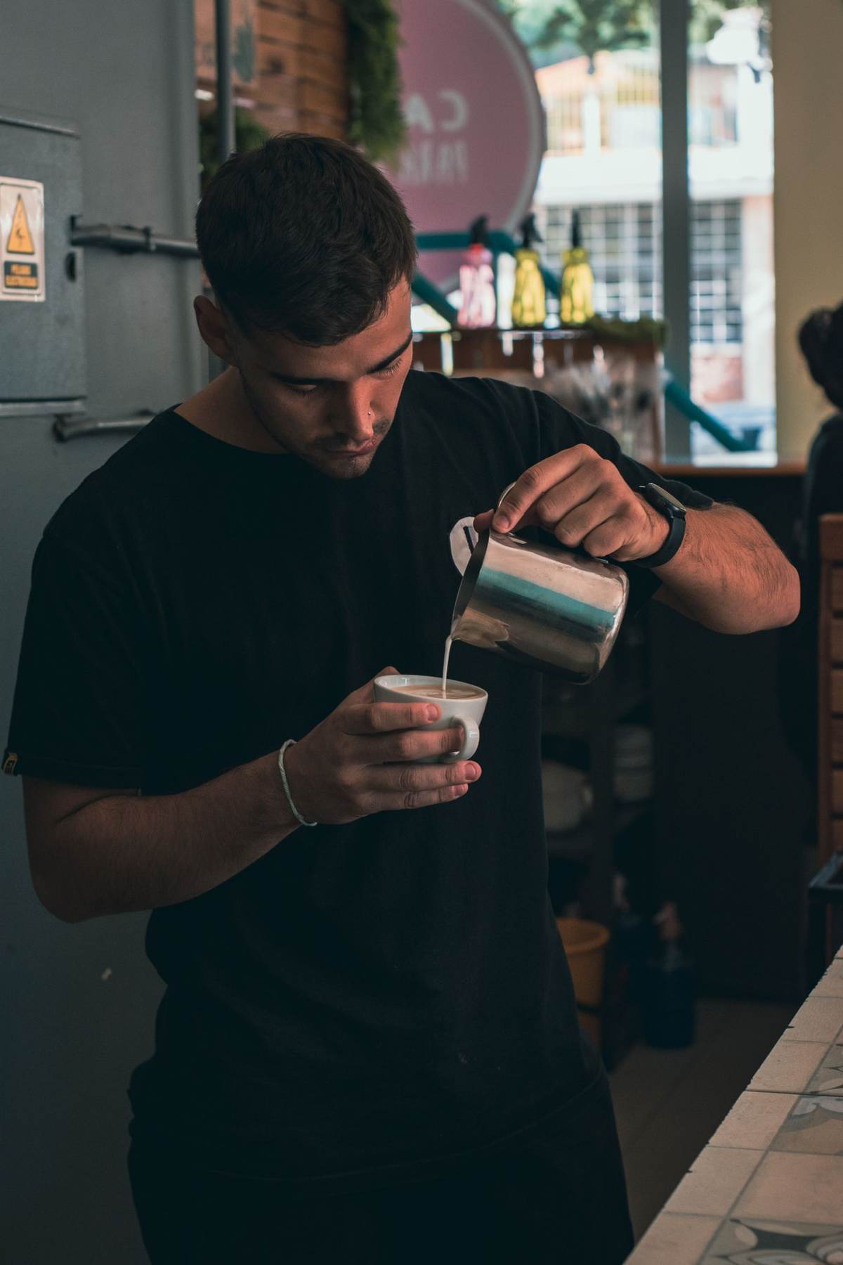 En barista hælder mælk i en kop bag disken