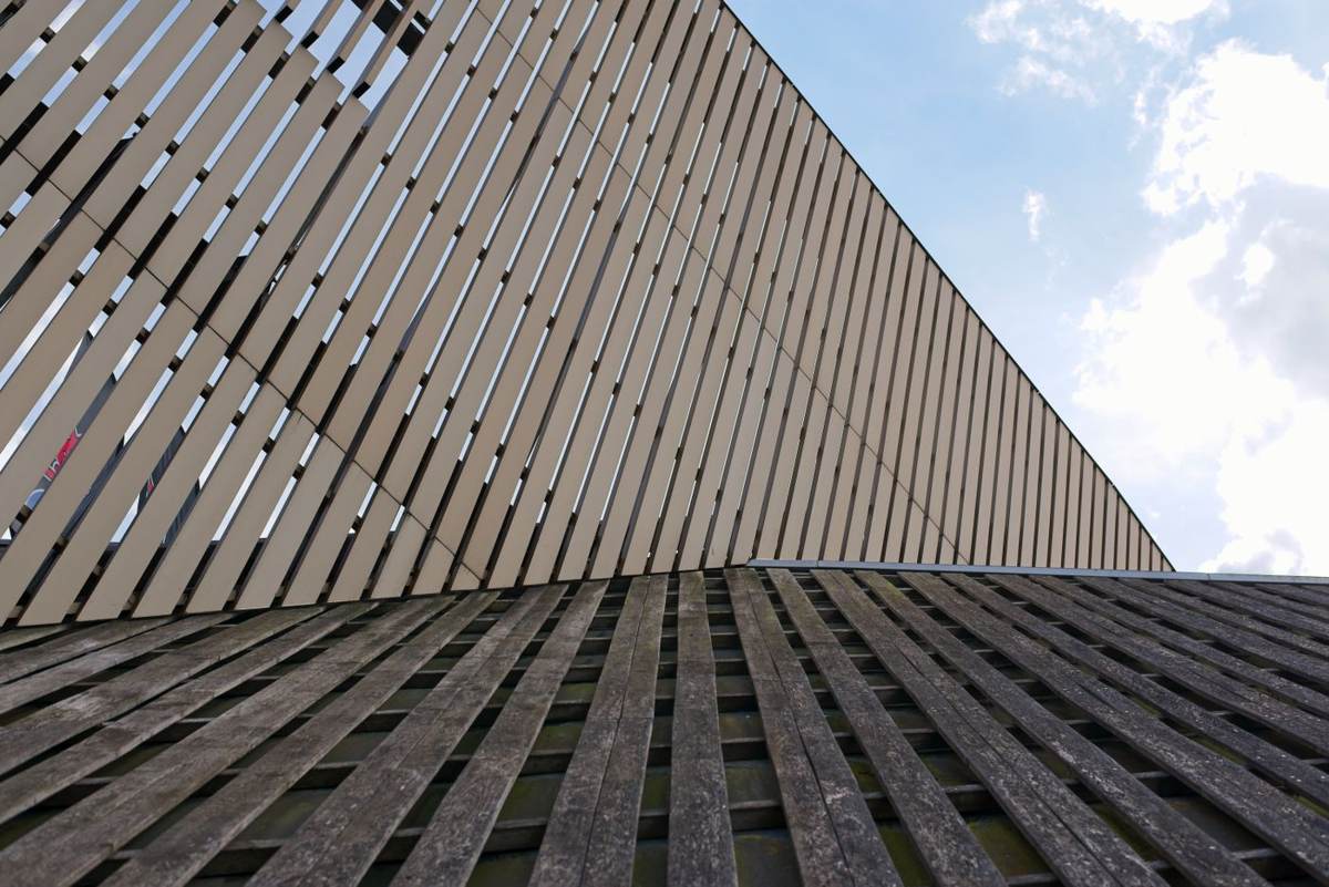 Set nedefra en facade af brune træspiler mod blå himmel med skyer