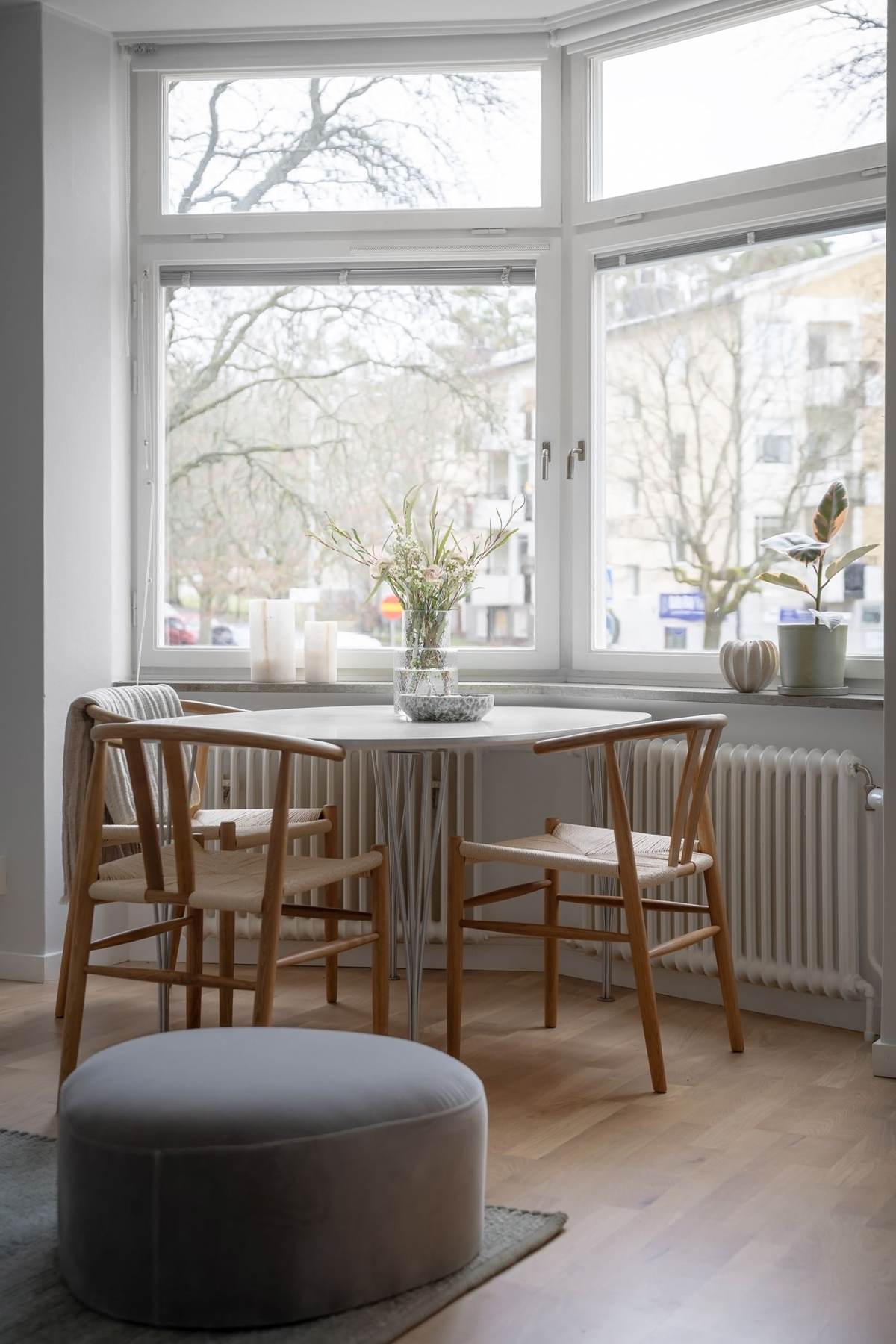 Et spisebord med stole foran store hjørnevinduer med udsigt til træer