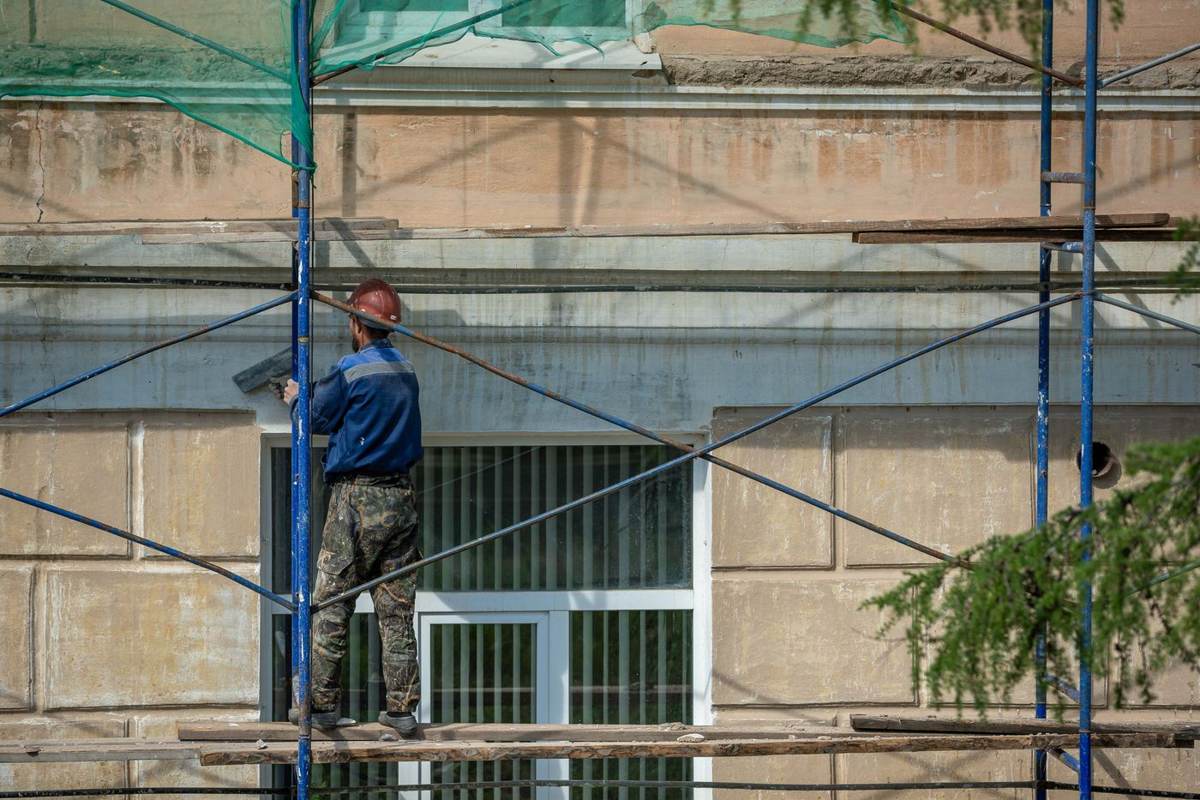 En arbejder klatrer på et stillads foran en beige facade