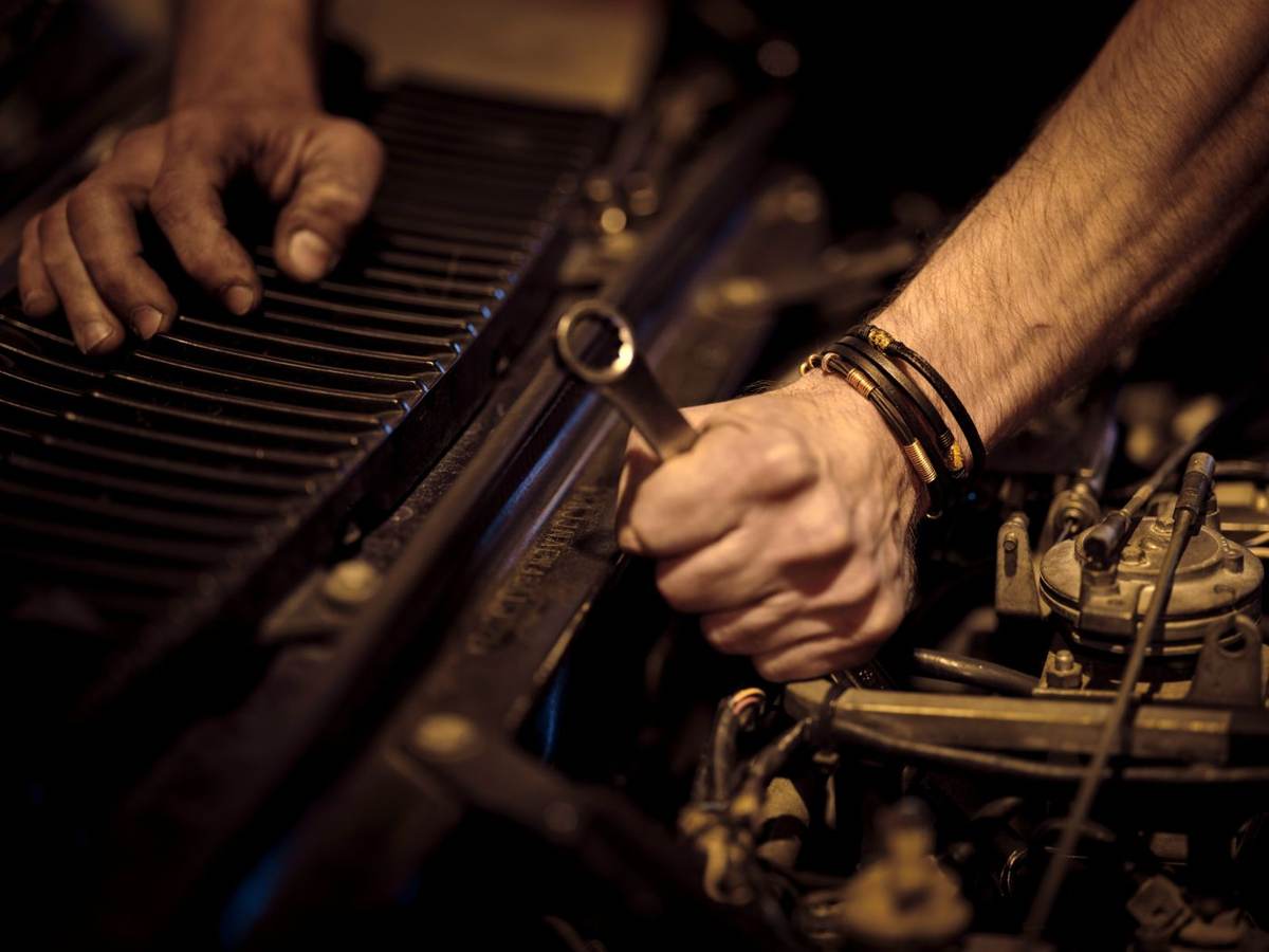 Nærbillede af hænder med armbånd, der skruer på en motor med en skruenøgle