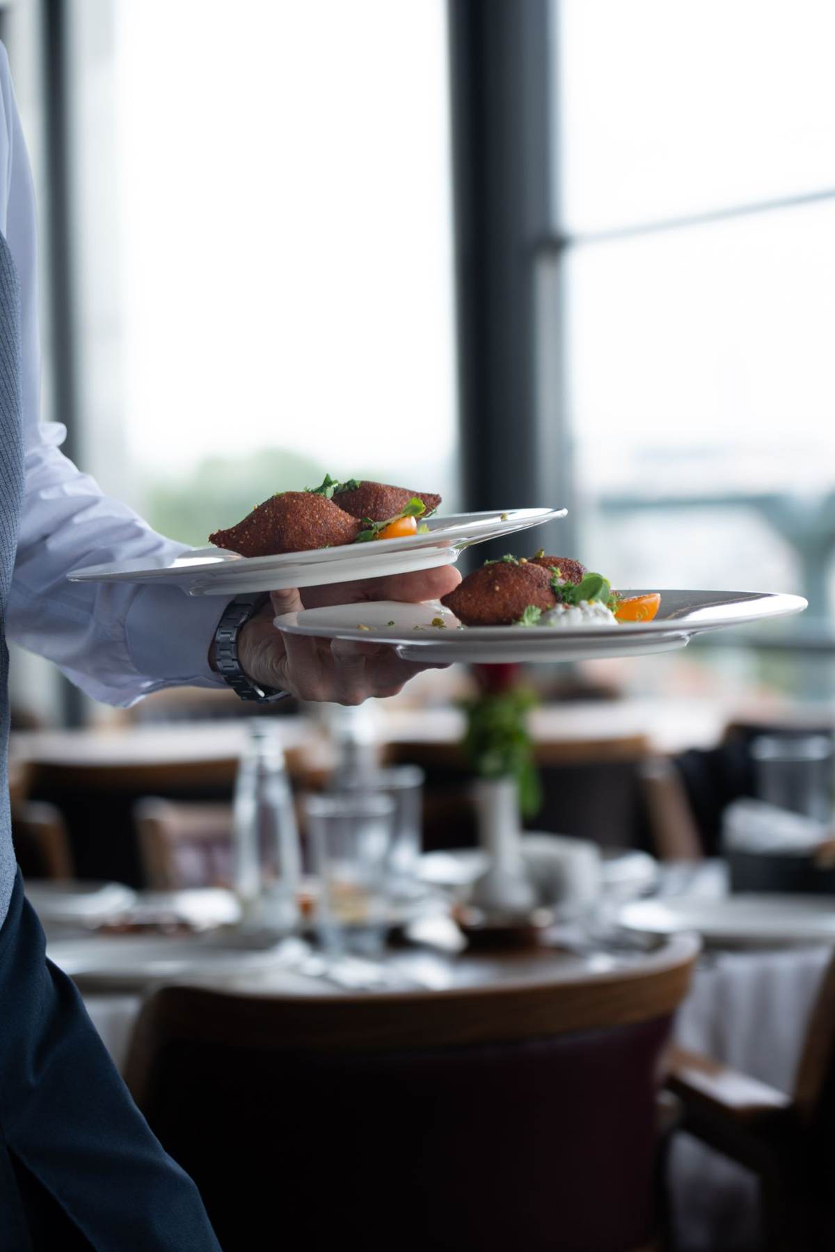 En tjener serverer tallerkener ved et dækket bord i en lys spisesal