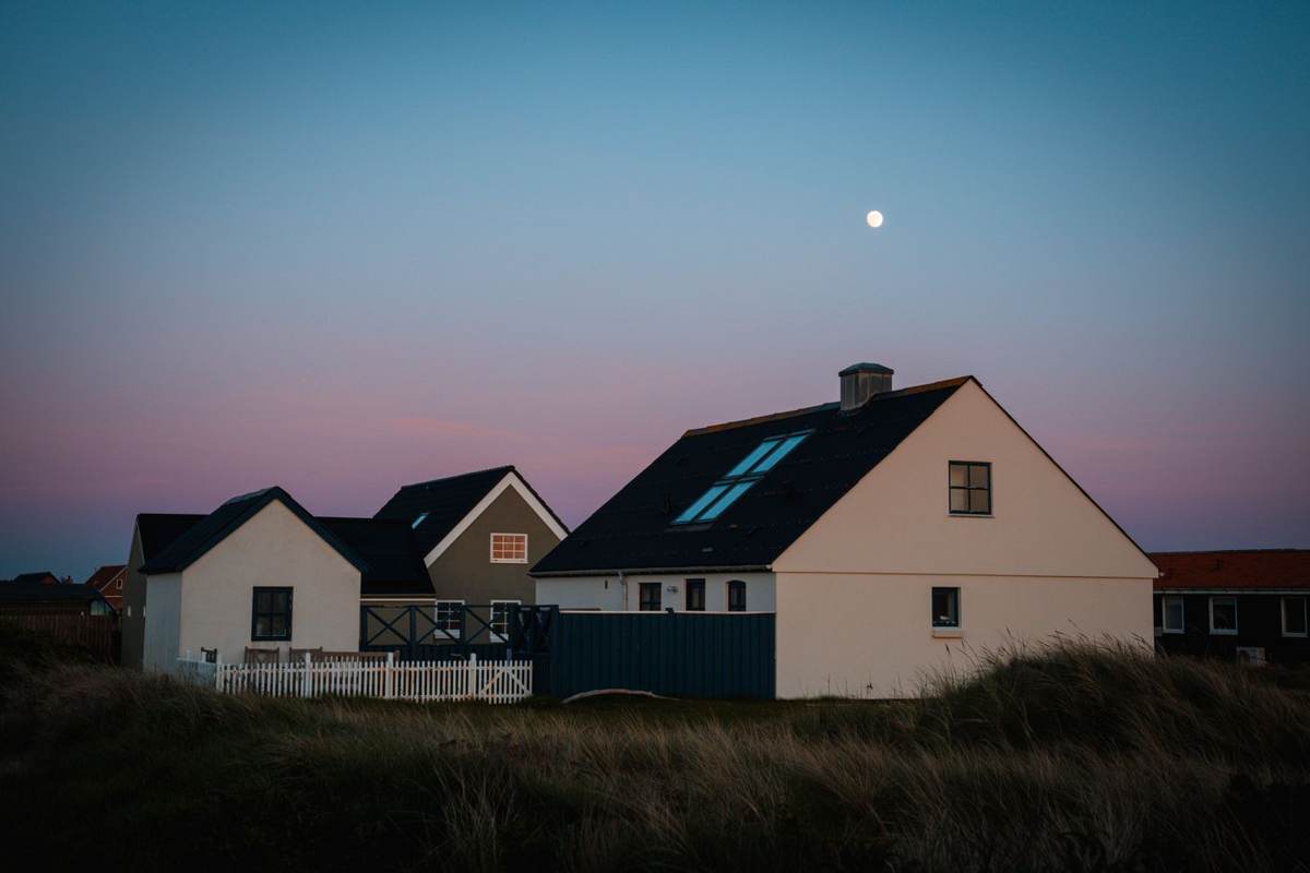 Hvide huse i klitterne under en lilla aftenhimmel med måne