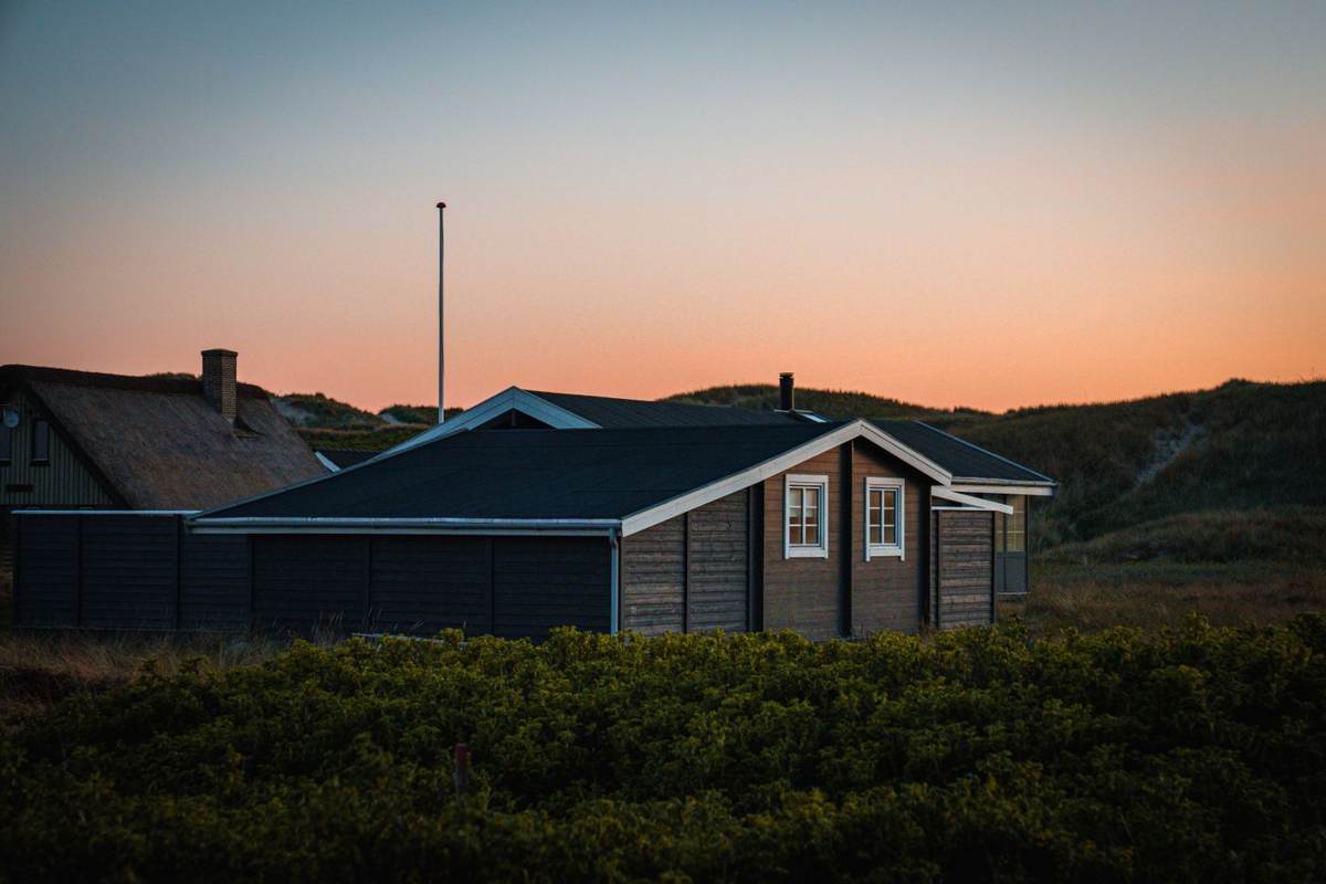Sommerhus i skumringen med orange lys på himlen og klitter bagved
