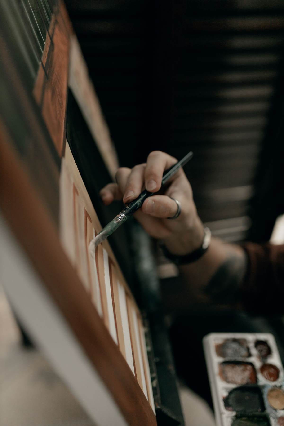 En hånd med pensel arbejder ved en palet i et mørkt atelier