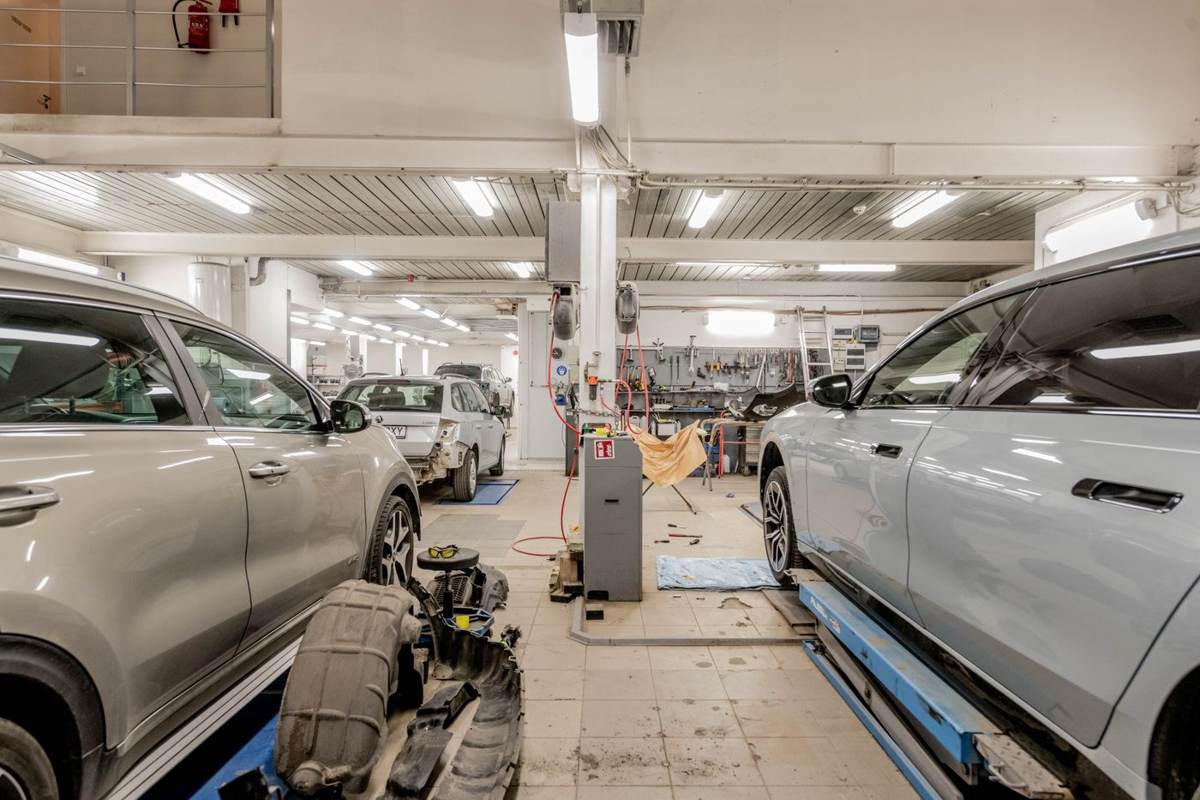 Lang, lys værkstedshal med biler på lifte