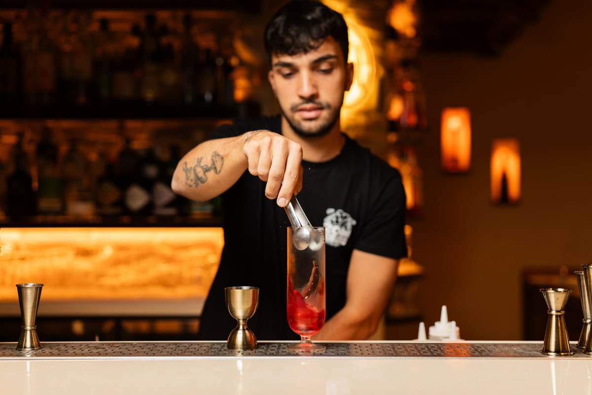 En bartender hælder en rød drink op bag en bardisk i varmt lys