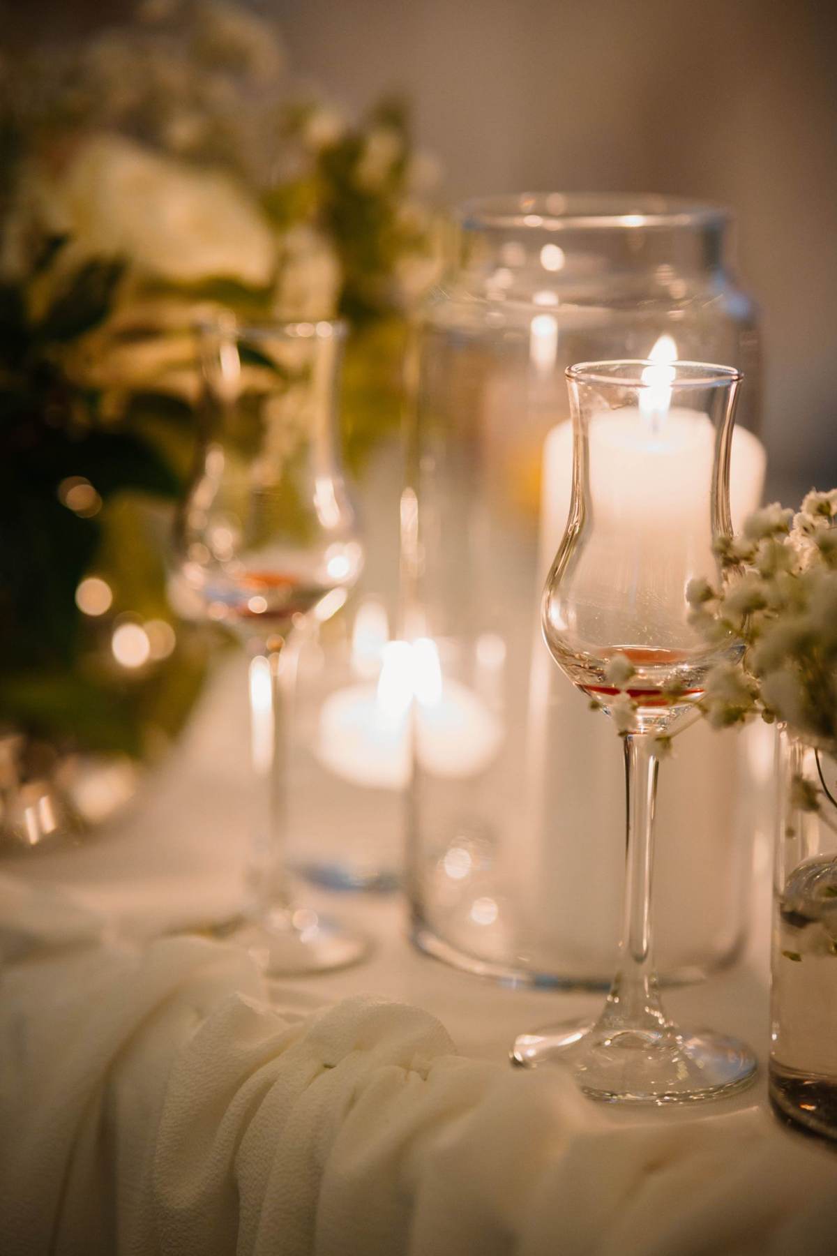 Stearinlys i glas og en blomsterdekoration på et bord med lys dug