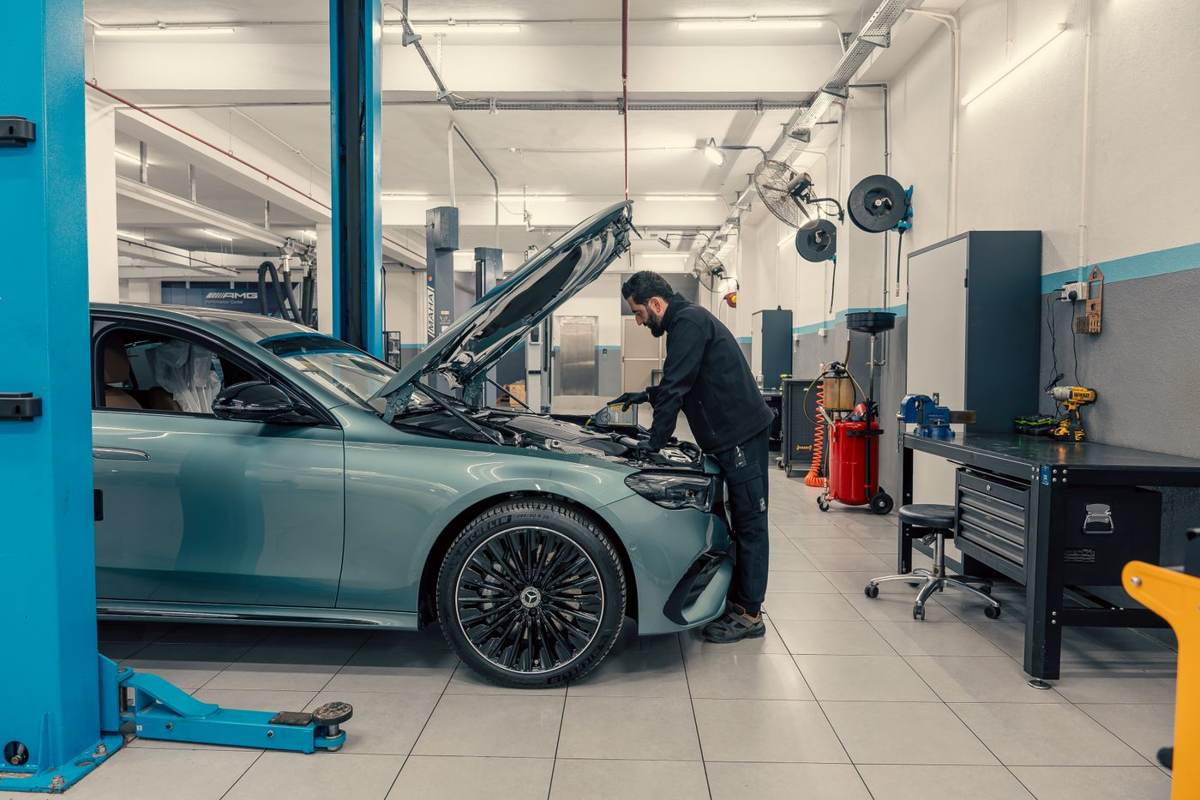 En mekaniker arbejder under åben motorhjelm i et lyst værksted med blå lifte