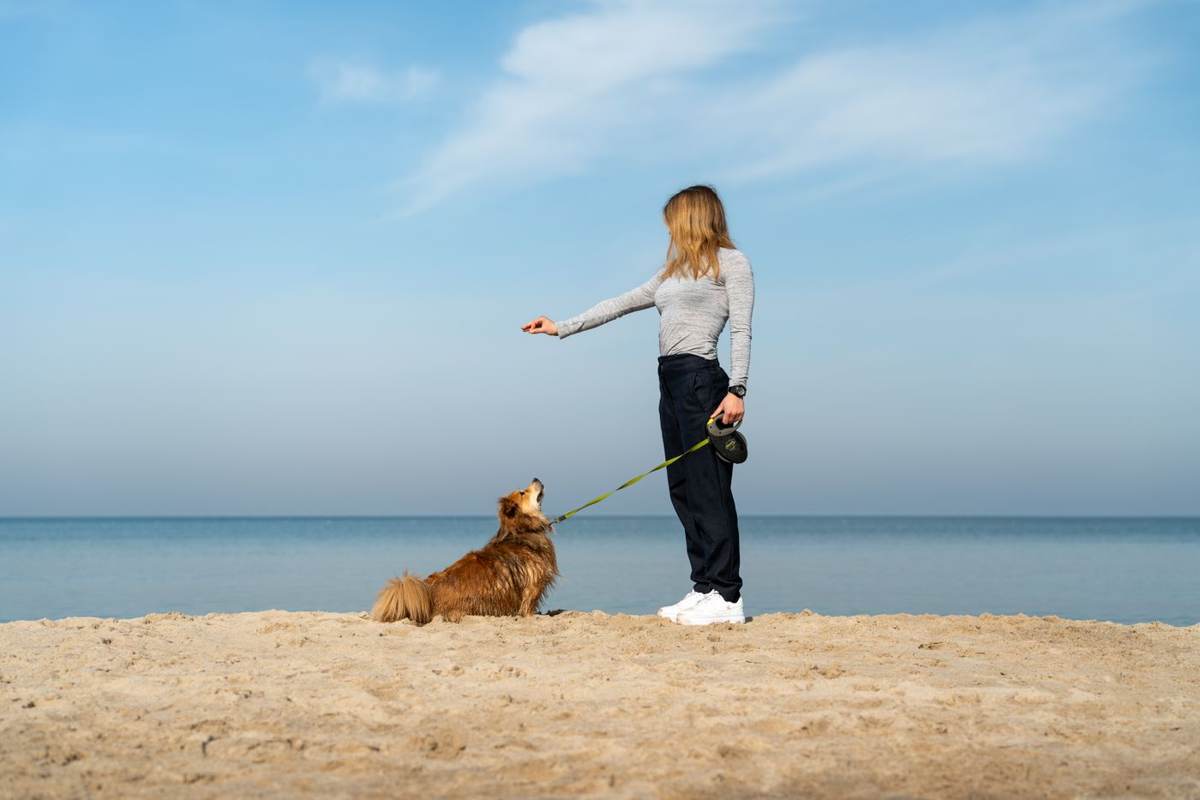 Kvinde står med en hund i snor på stranden