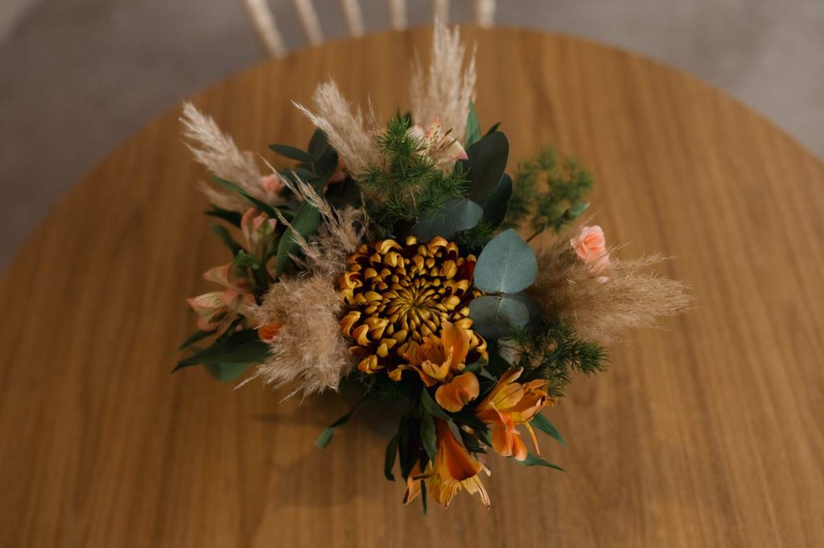 En rund buket med tørrede blomster og pampasgræs set ovenfra på et træbord