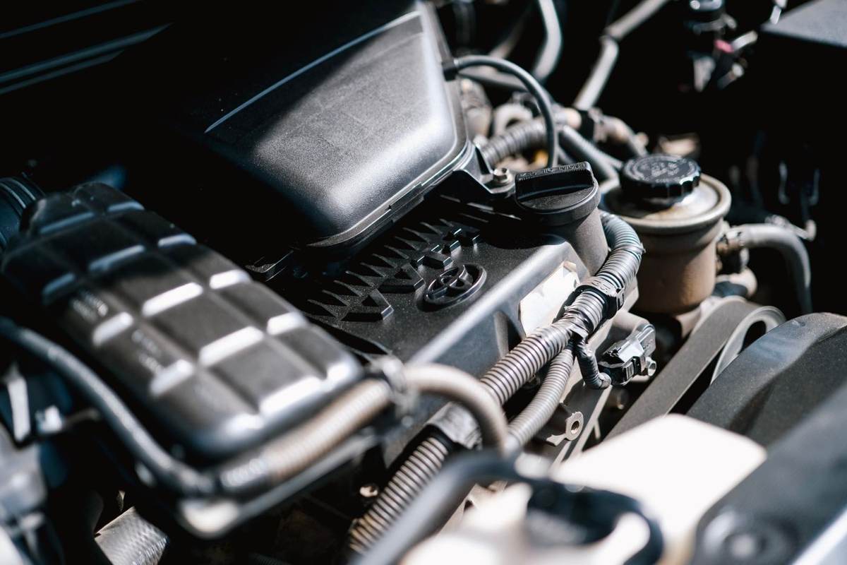 Tæt på en bilmotor med slanger, ledninger og et sort motordæksel