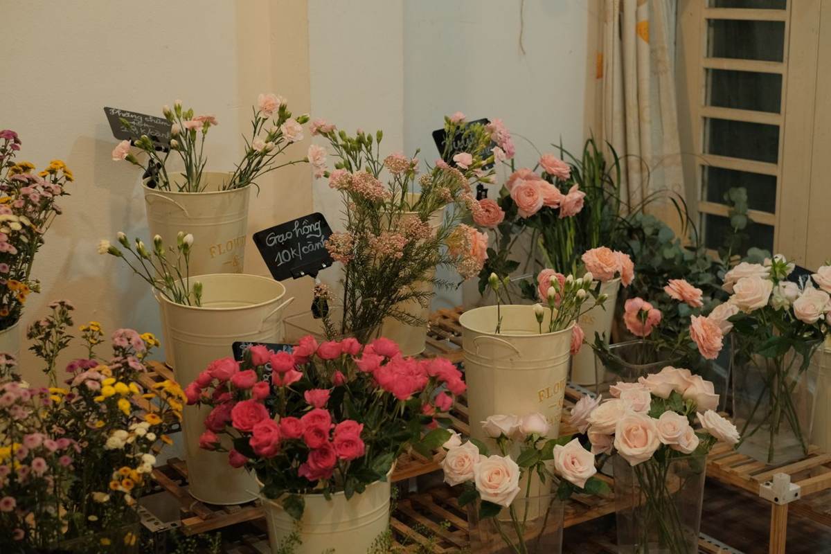 Spande med lyserøde og gule blomster i en butik med en lille tavle