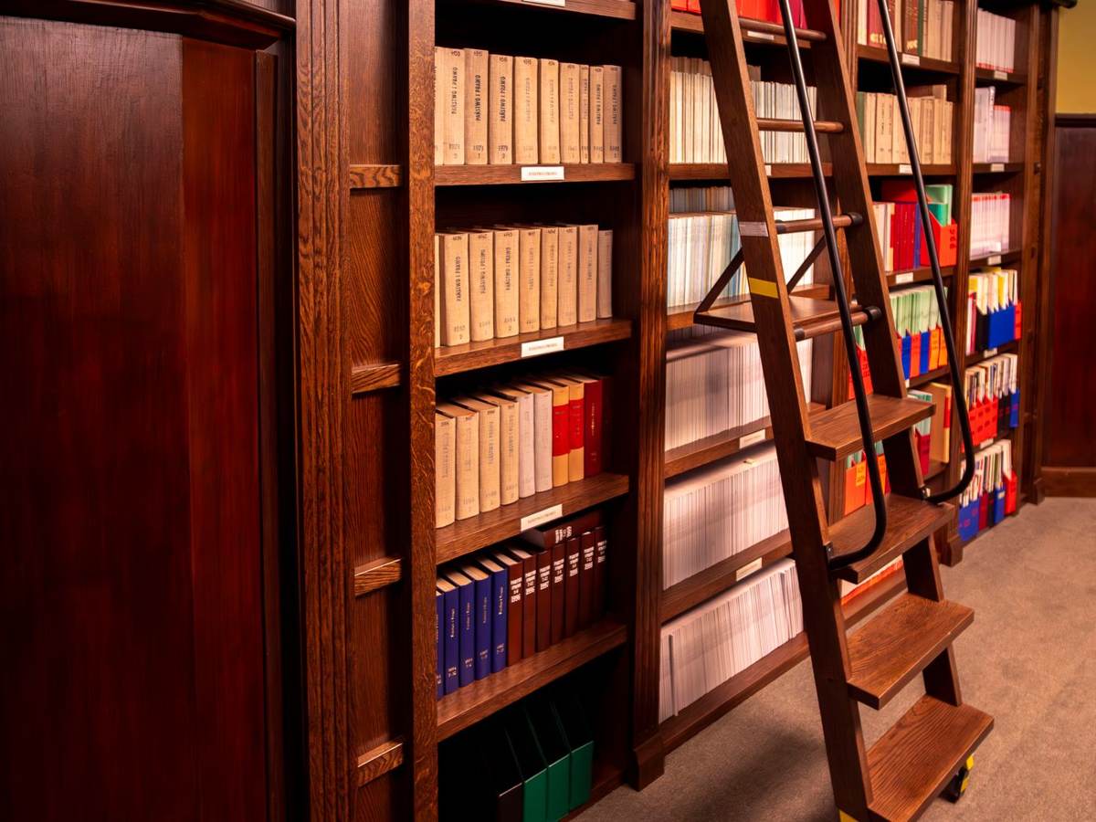 Mørke træreoler med bøger og en rullestige i et gammelt bibliotek