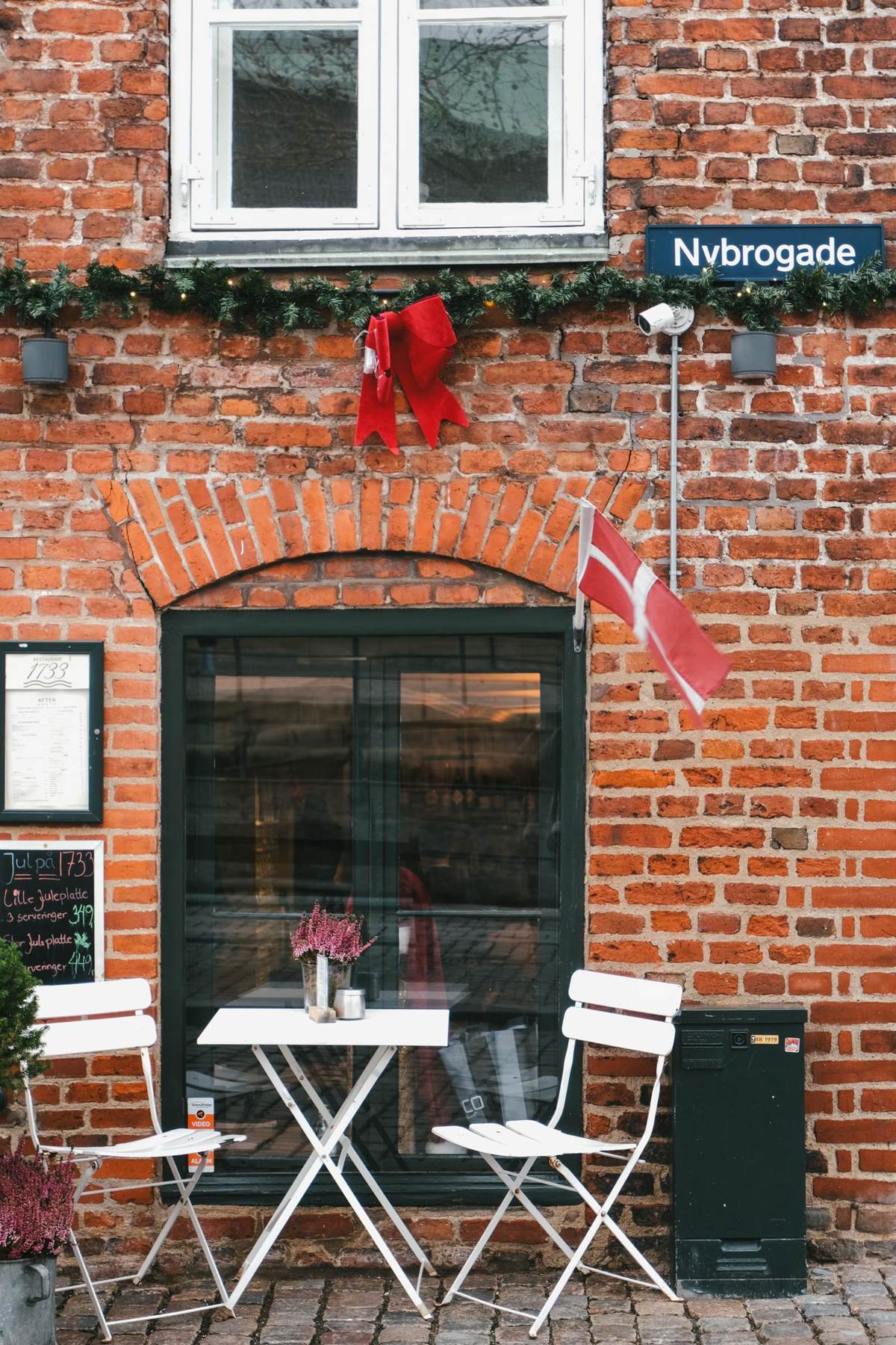 Udendørs café-bord og klapstole foran en murstensfacade
