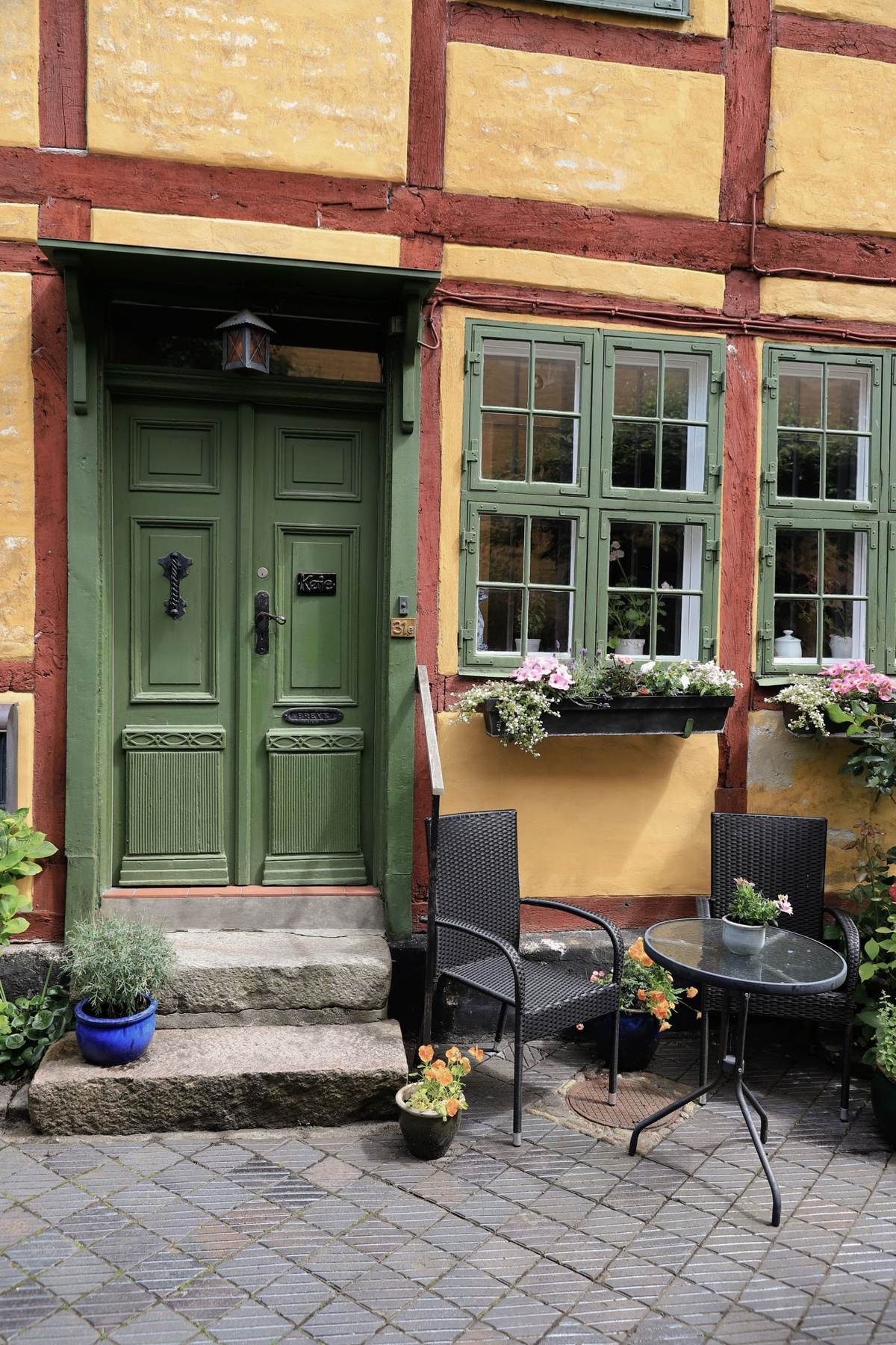 En grøn dør og vinduer med blomsterkasser i en gammel bindingsværksbygning