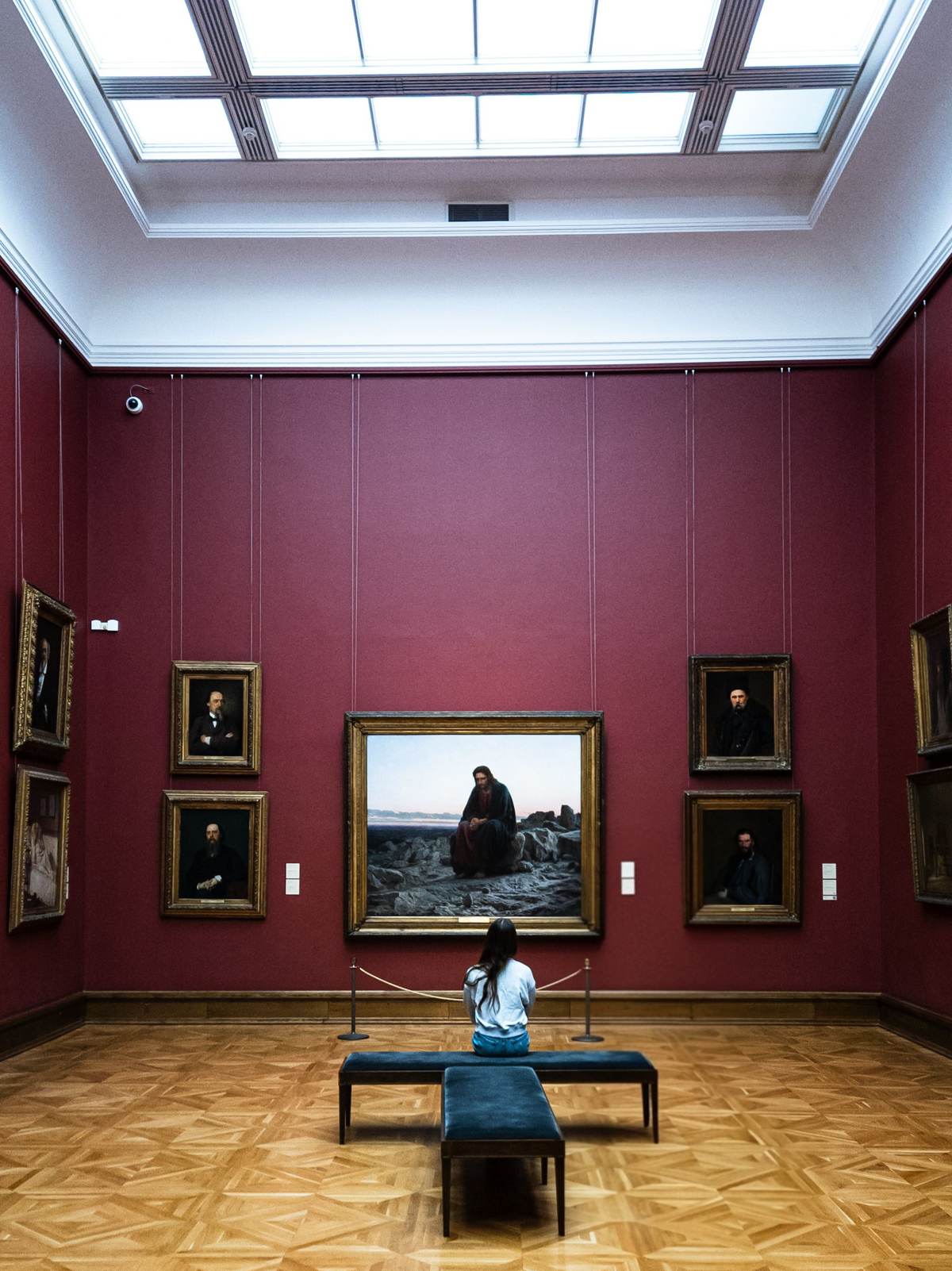 En person på en bænk i et rødt galleri med lys fra ovenlyset