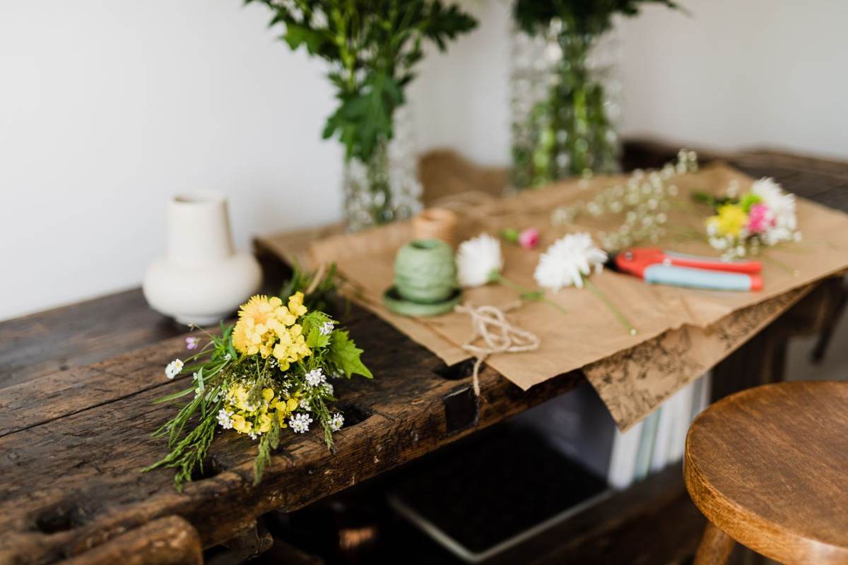 Et gammelt træbord med papir, blomster og vaser i lyst rum