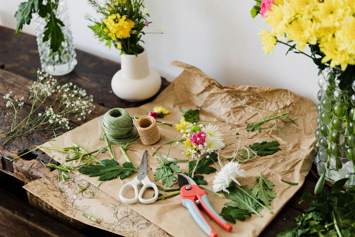 Papir, snor, sakse og friske blomster ligger på et bord set ovenfra