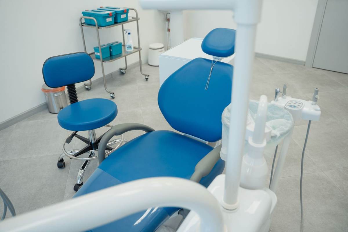 Blå behandlerstol og lampe set fra siden i et lyst klinikrum