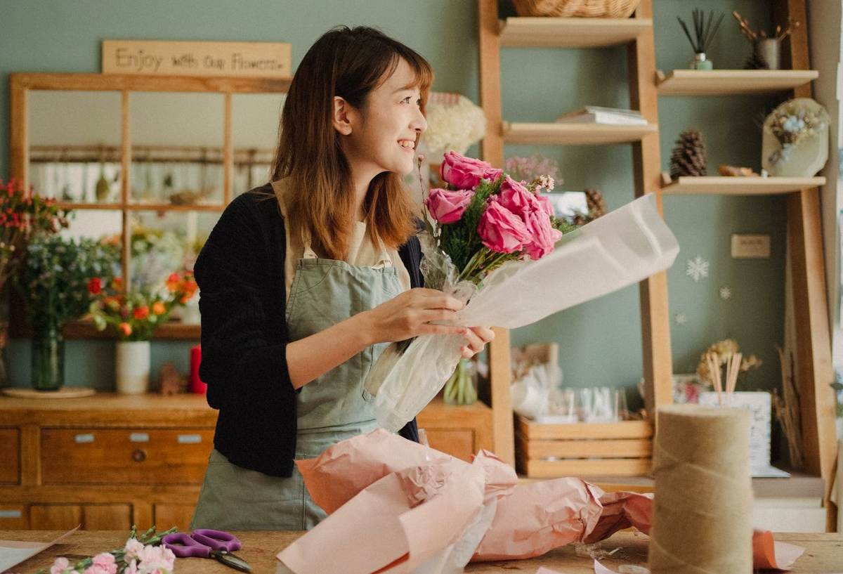 En kvinde i forklæde pakker en lyserød buket ind i papir i en blomsterbutik
