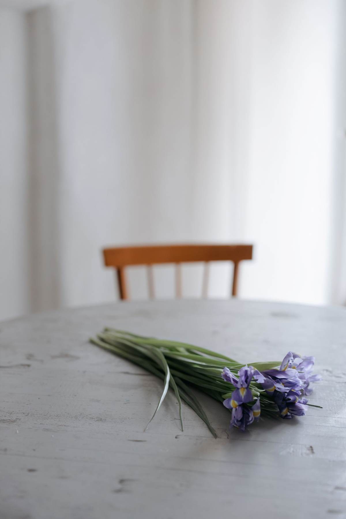 Et lille bundt blå og lilla blomster ligger på et gråt bord foran en træstol