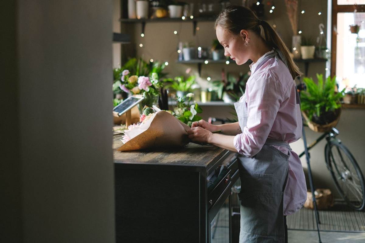 En blomsterbinder står ved en arbejdsbænk i et mørkt værksted og pakker en buket