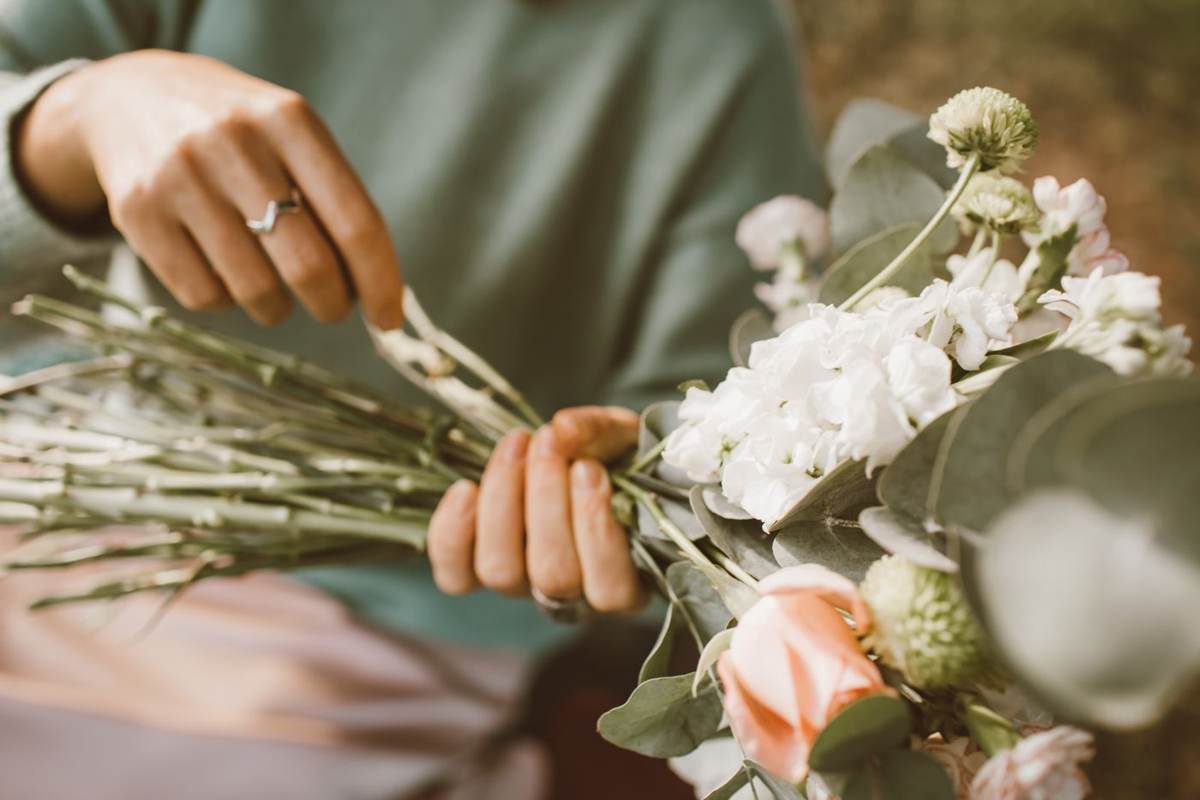 Hænder holder en løs buket med hvide og ferskenfarvede blomster