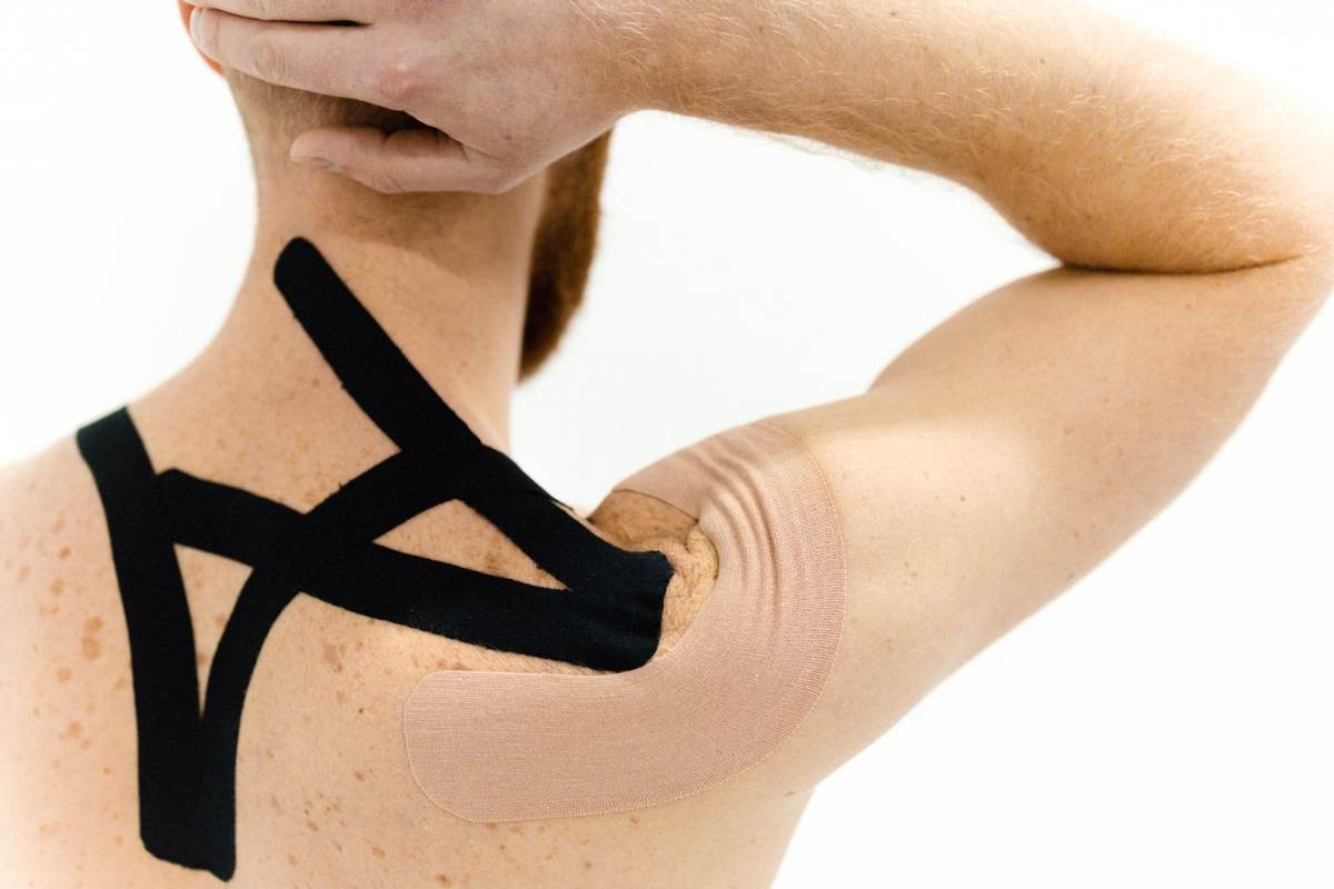 Skulder og overarm med sort kinesiotape mod hvid baggrund