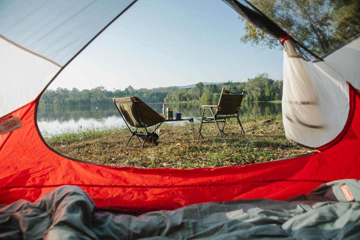 Udsigt ud af et rødt telt mod en sø og to campingstole