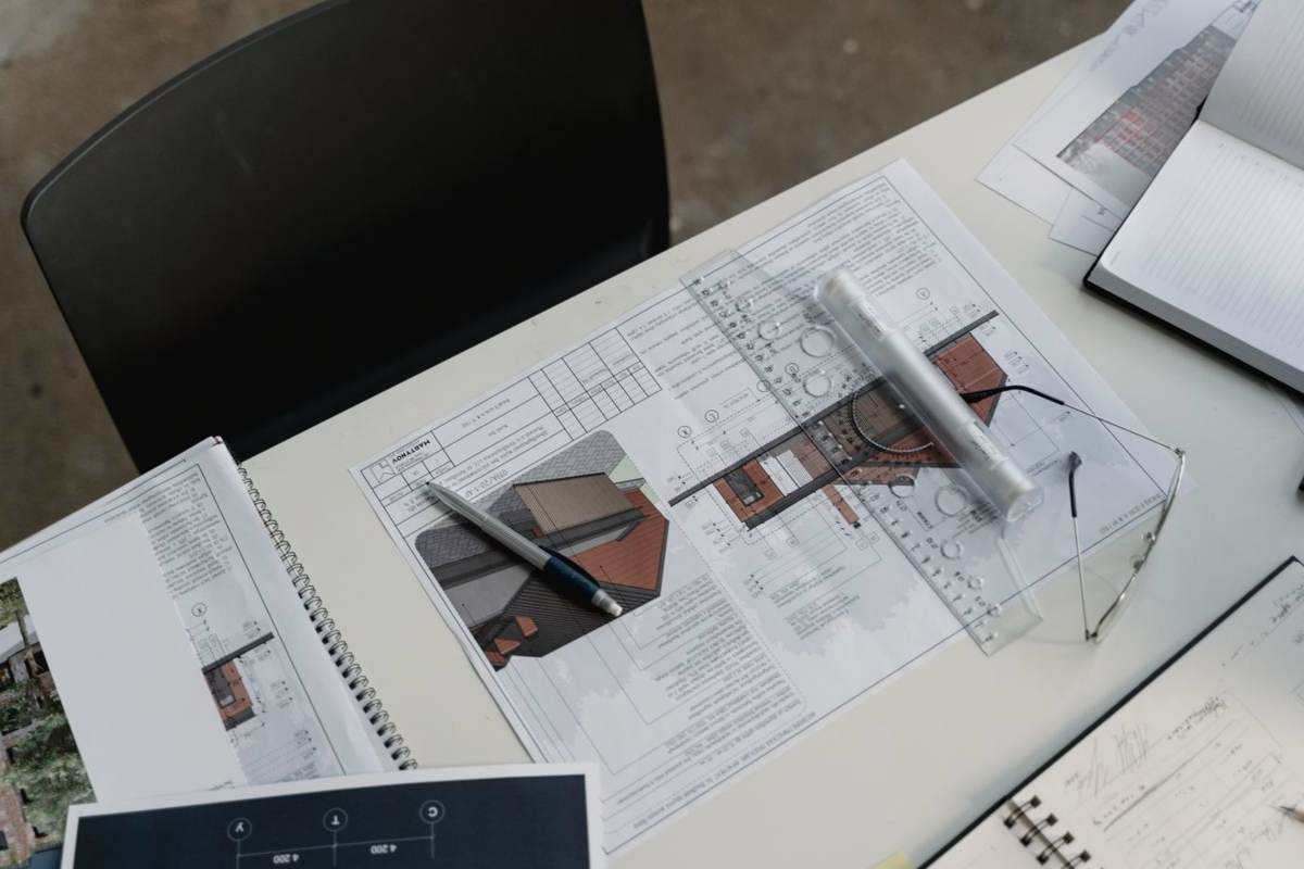 Set oppefra ligger tegninger og små modeller på et hvidt arbejdsbord