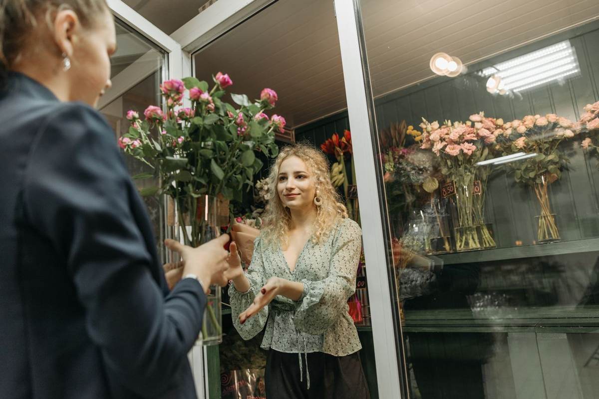 En kunde og en blomsterhandler taler sammen foran en kølemontre med roser