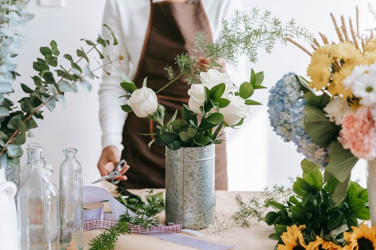 En person i forklæde arrangerer blomster i metalspande og glasflasker