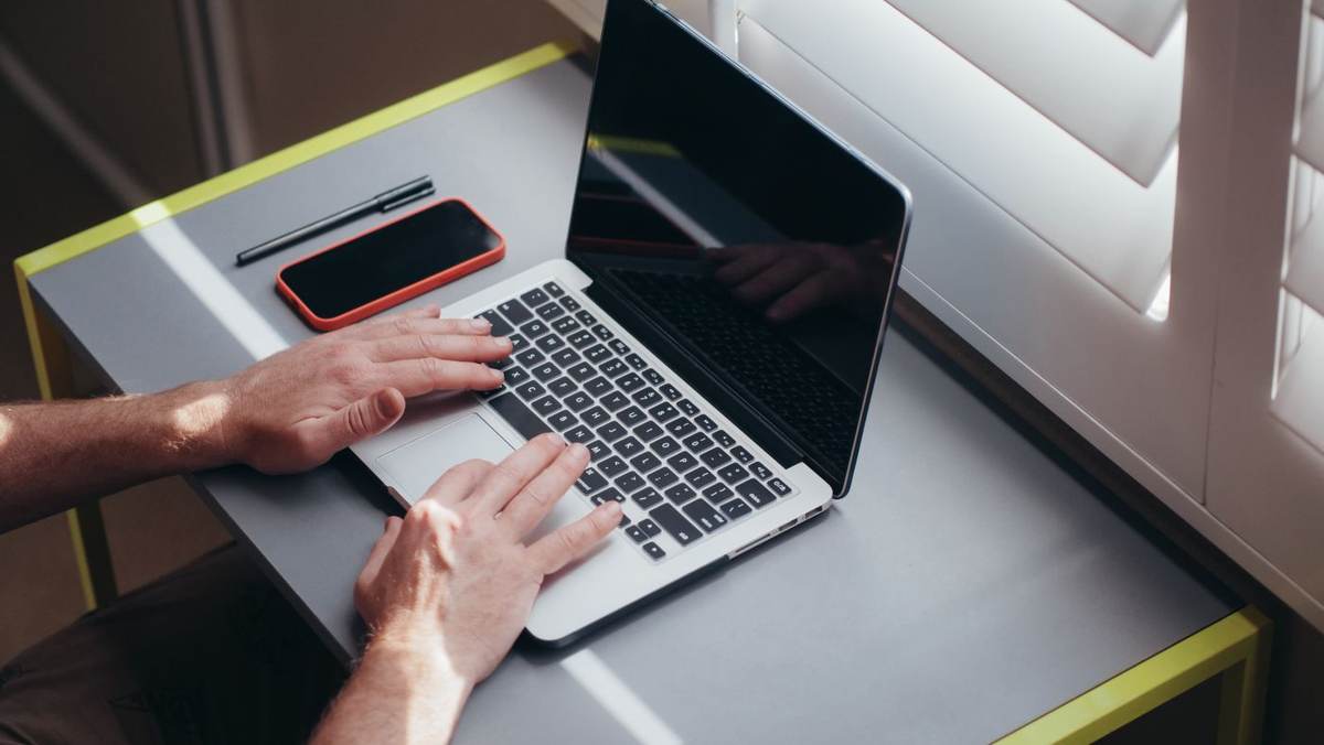 To hænder skriver på en bærbar computer ved siden af en telefon og en pen
