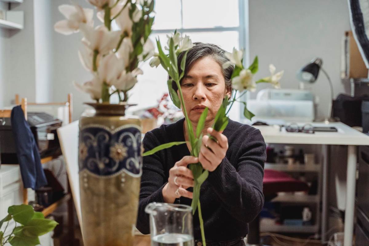 En ældre kvinde arrangerer en lang stilk i en vase ved et værkstedsbord