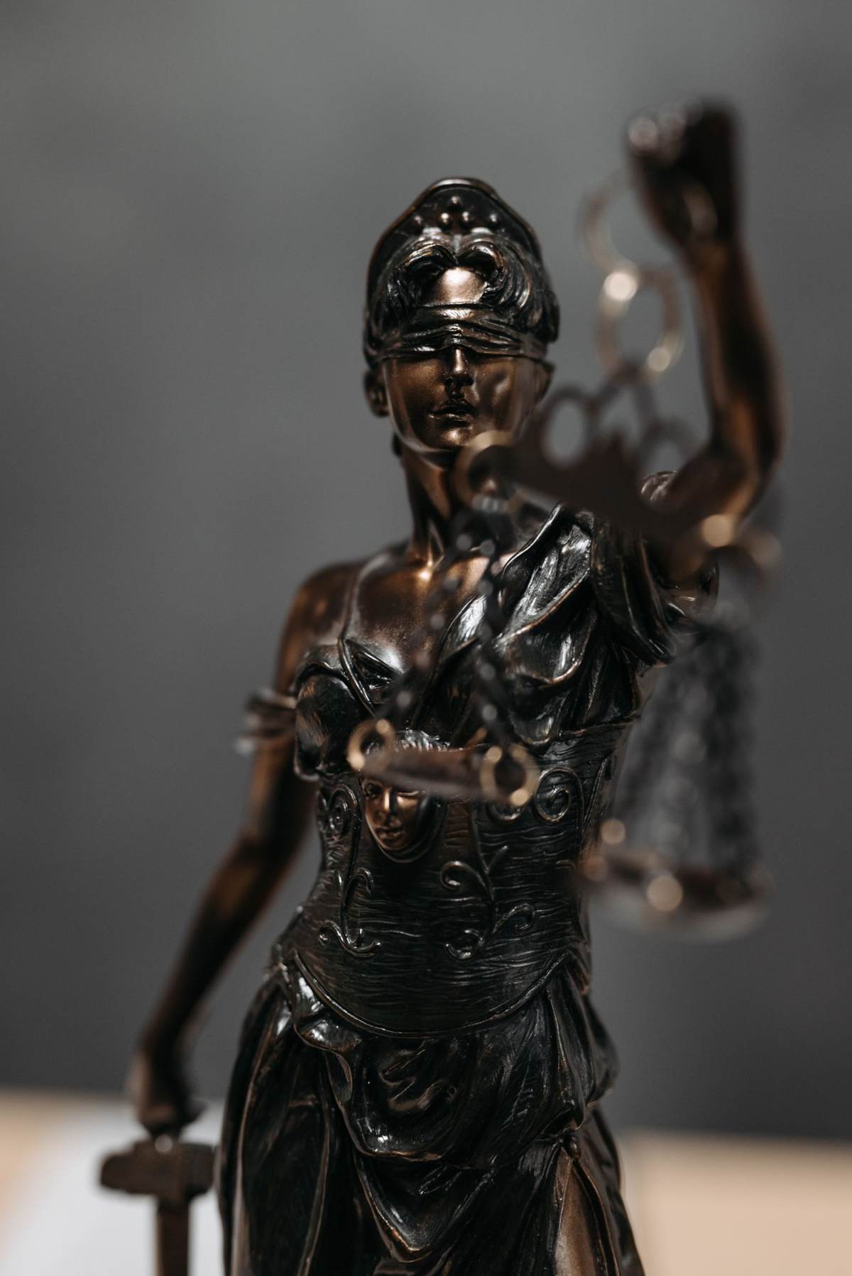 Bronzestatue af retfærdighedsgudinden med vægt og sværd foran grå baggrund