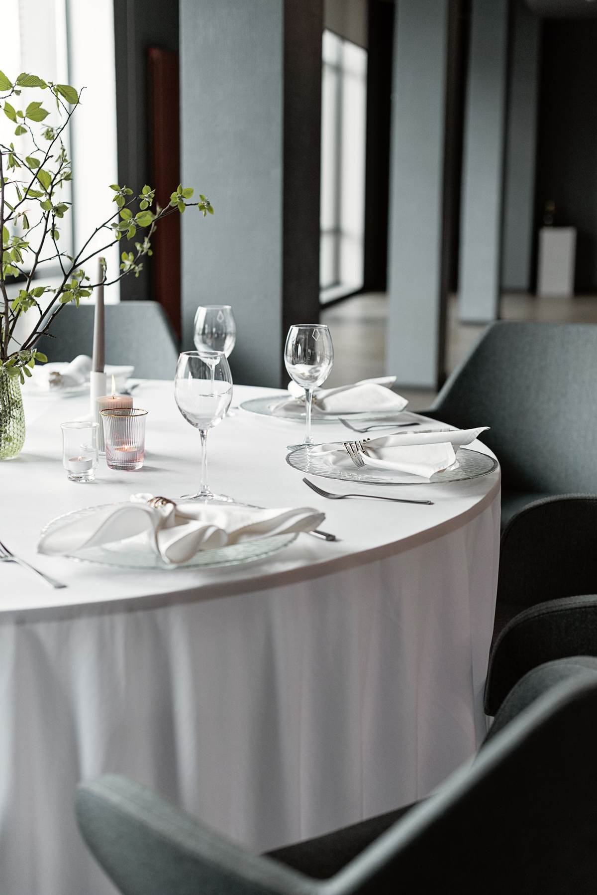 Dækket rundt bord med vinglas og bestik i en lys restaurant