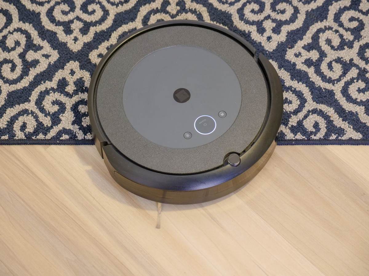 En robotstøvsuger set ovenfra på et trægulv ved et mønstret tæppe