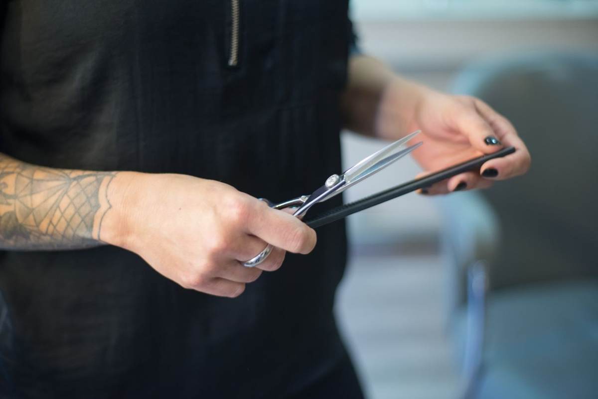 Barber med tatoverede hænder holder saks og kam
