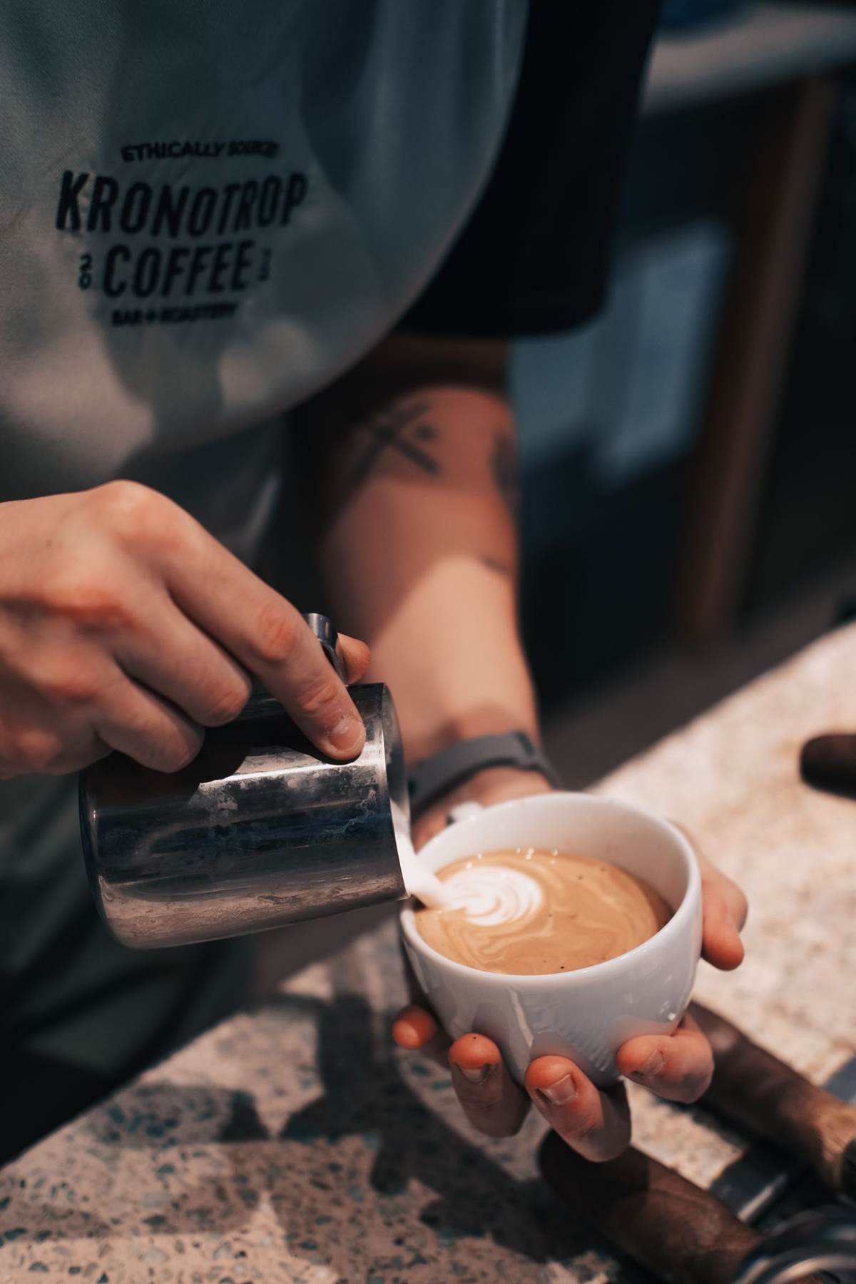 Hænder hælder dampet mælk i en kop kaffe