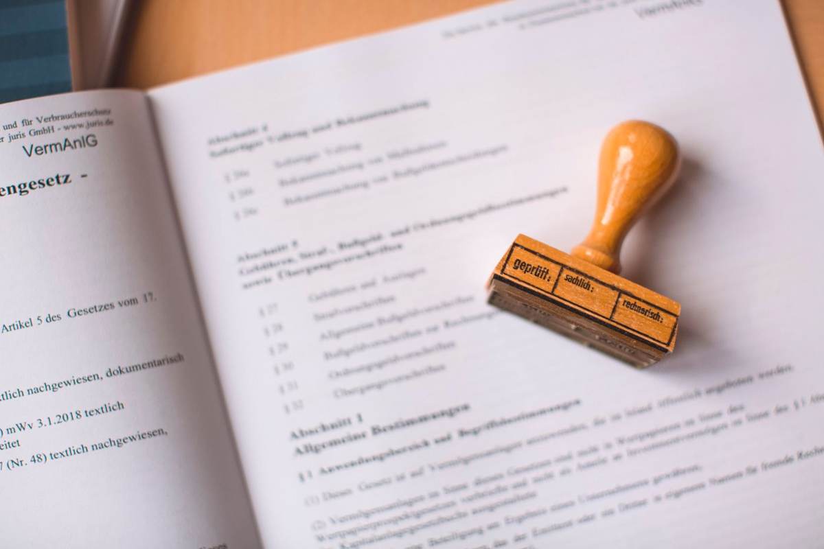Et træstempel ligger på en opslået tekst med små paragraffer