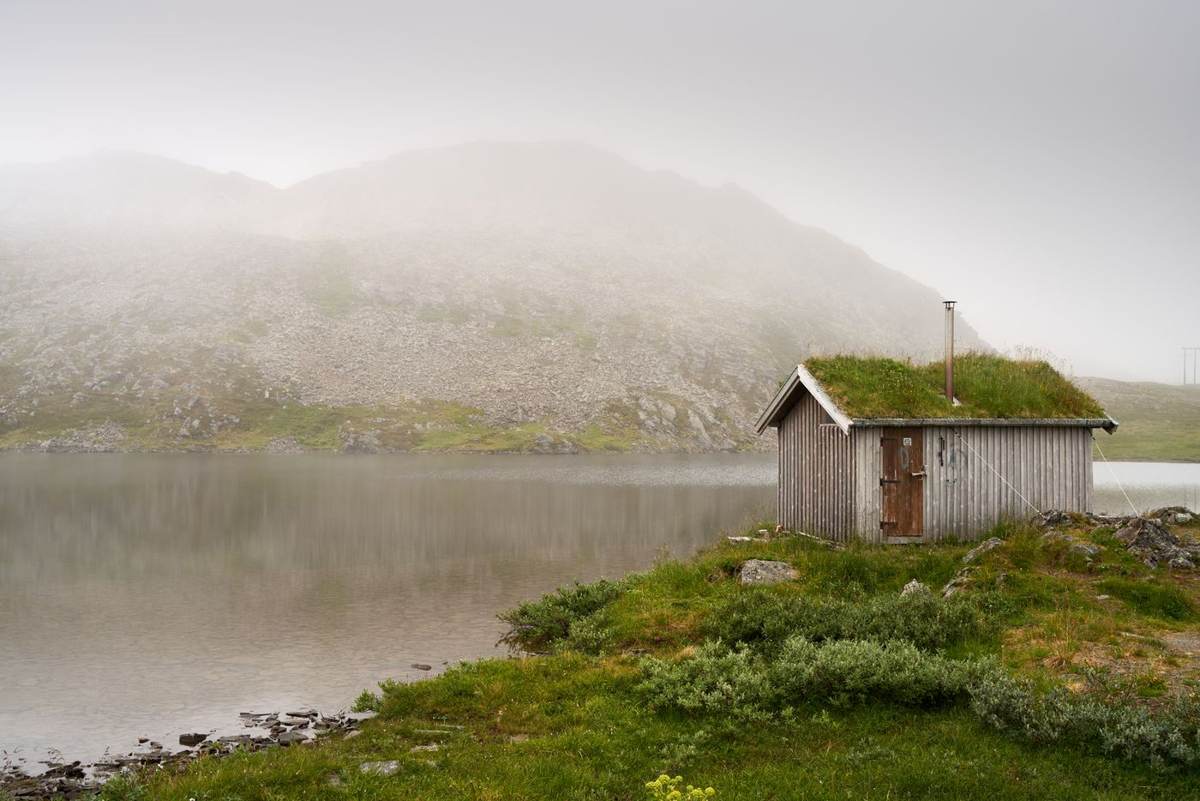 Lille hytte med tørvetag ved en rolig sø i tåge